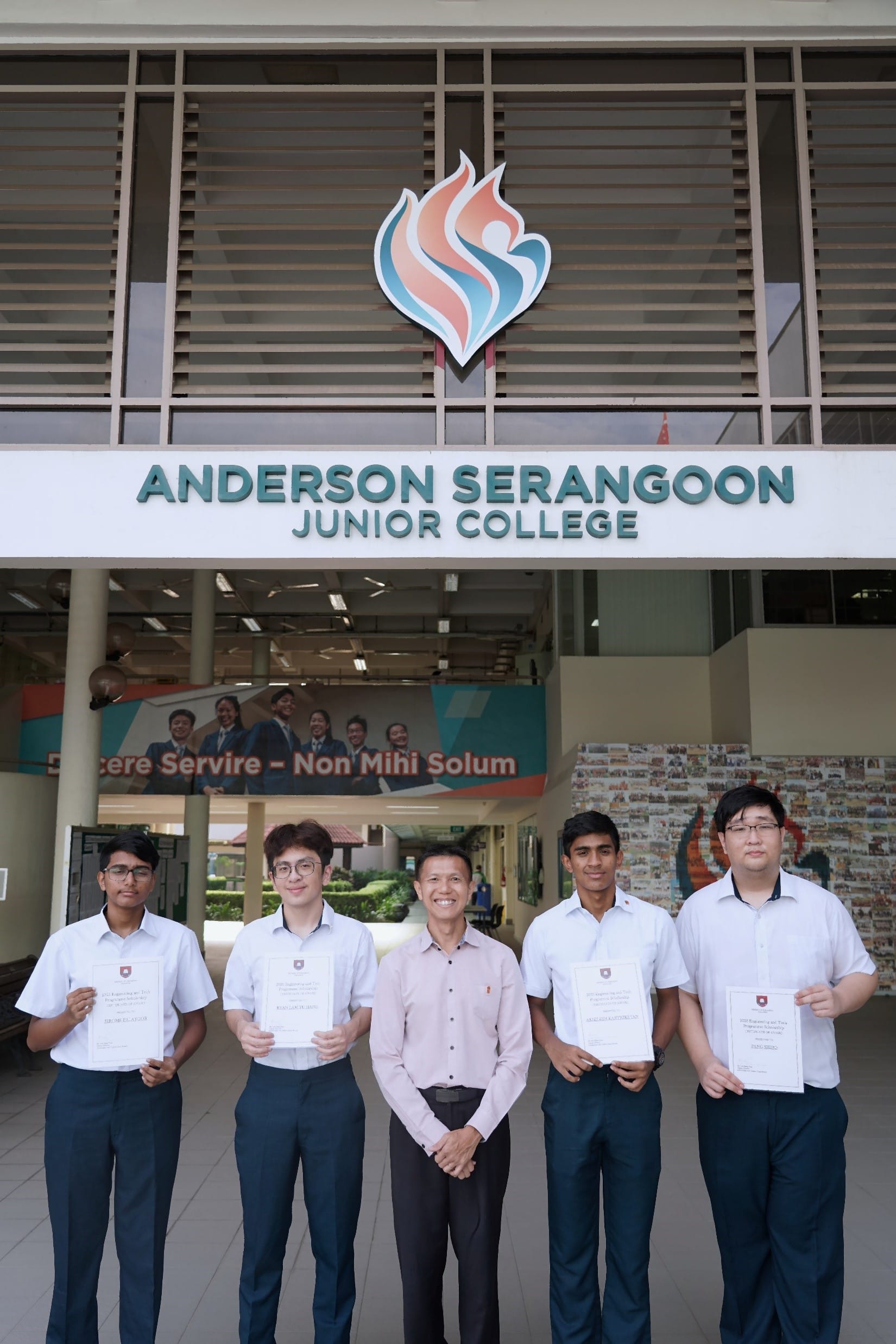 Five people pose with certificates in front of Anderson Serangoon Junior College building entrance.
